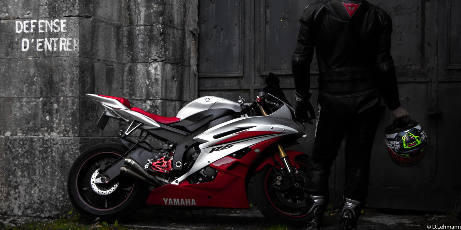 Man in Black Jacket and Black Pants Standing Beside Red and White Sports Bike. Wallpaper in 2048x1024 Resolution