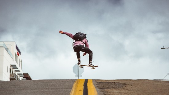 Image man in black jacket and black pants doing stunts on gray asphalt road under blue and