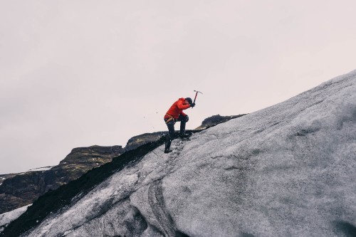 Image person in red jacket and black pants standing on gray rock mountain during daytime