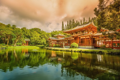 Image brown and white temple near green trees and lake under cloudy sky during daytime