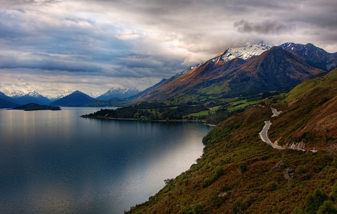 lake in the middle of green and brown mountains under white clouds