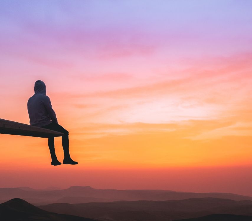 silhouette of man sitting on rock during sunset