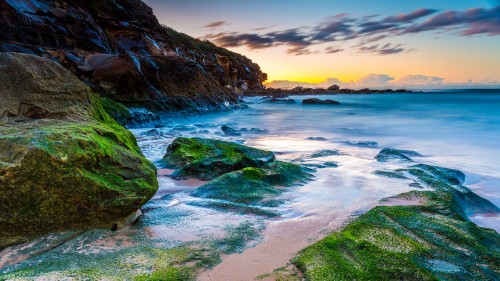 Image green and brown rock formation on sea shore during sunset