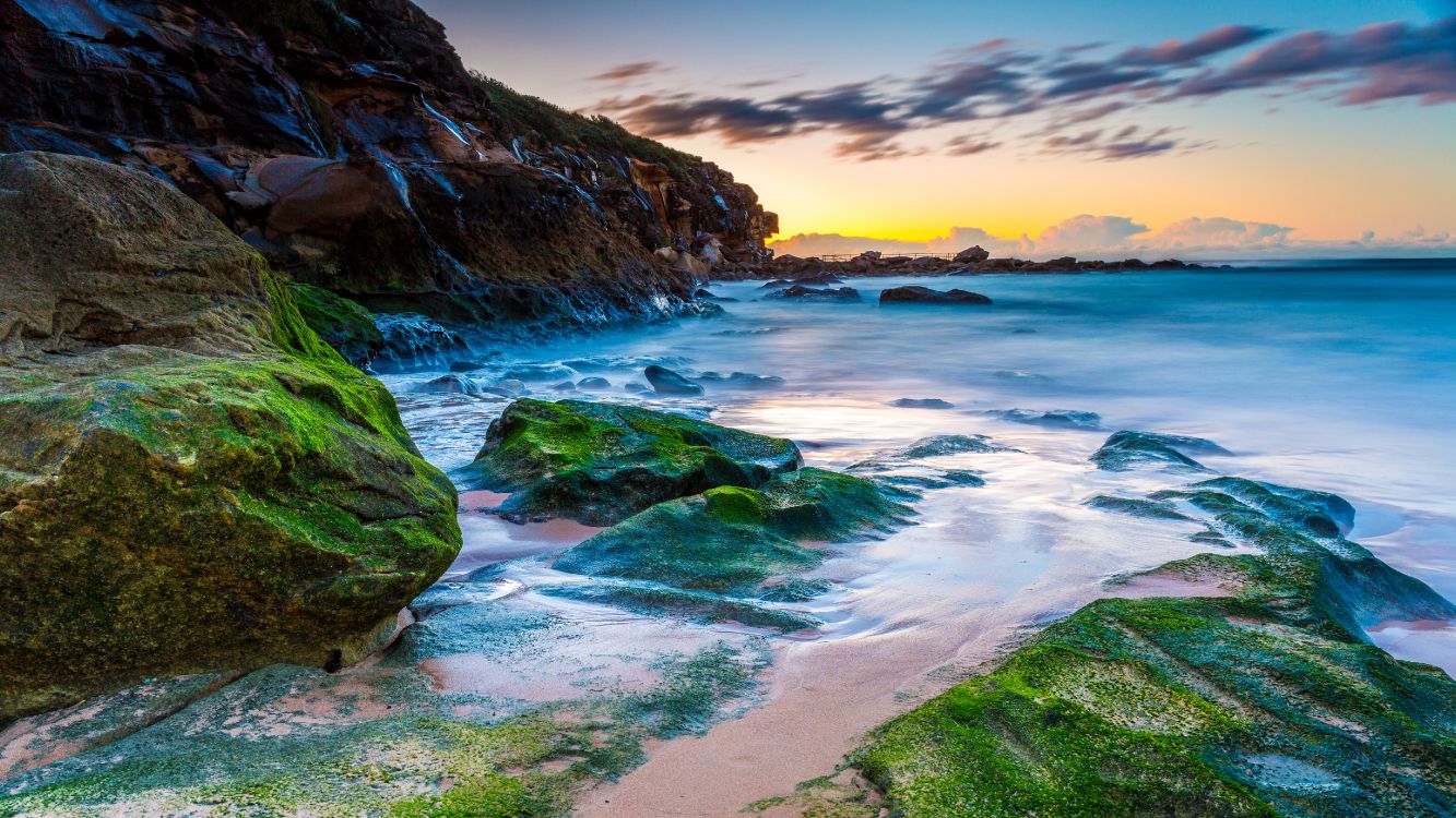 green and brown rock formation on sea shore during sunset