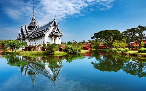 Image white and black house near green trees and body of water under blue sky during daytime