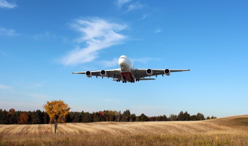 Image white and blue airplane flying over brown grass field during daytime