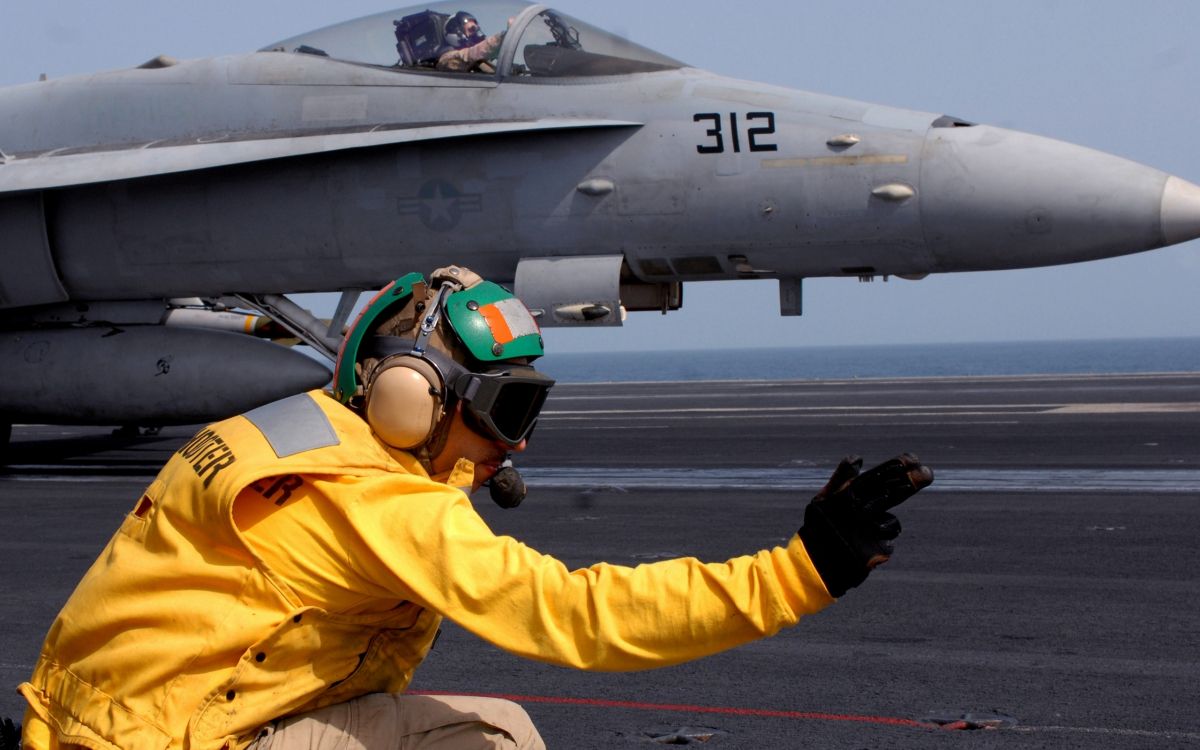 man in yellow jacket and helmet riding on gray jet plane